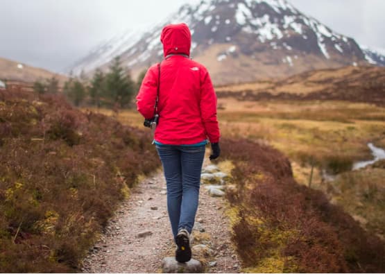 person with hood up walking on path towards mountain