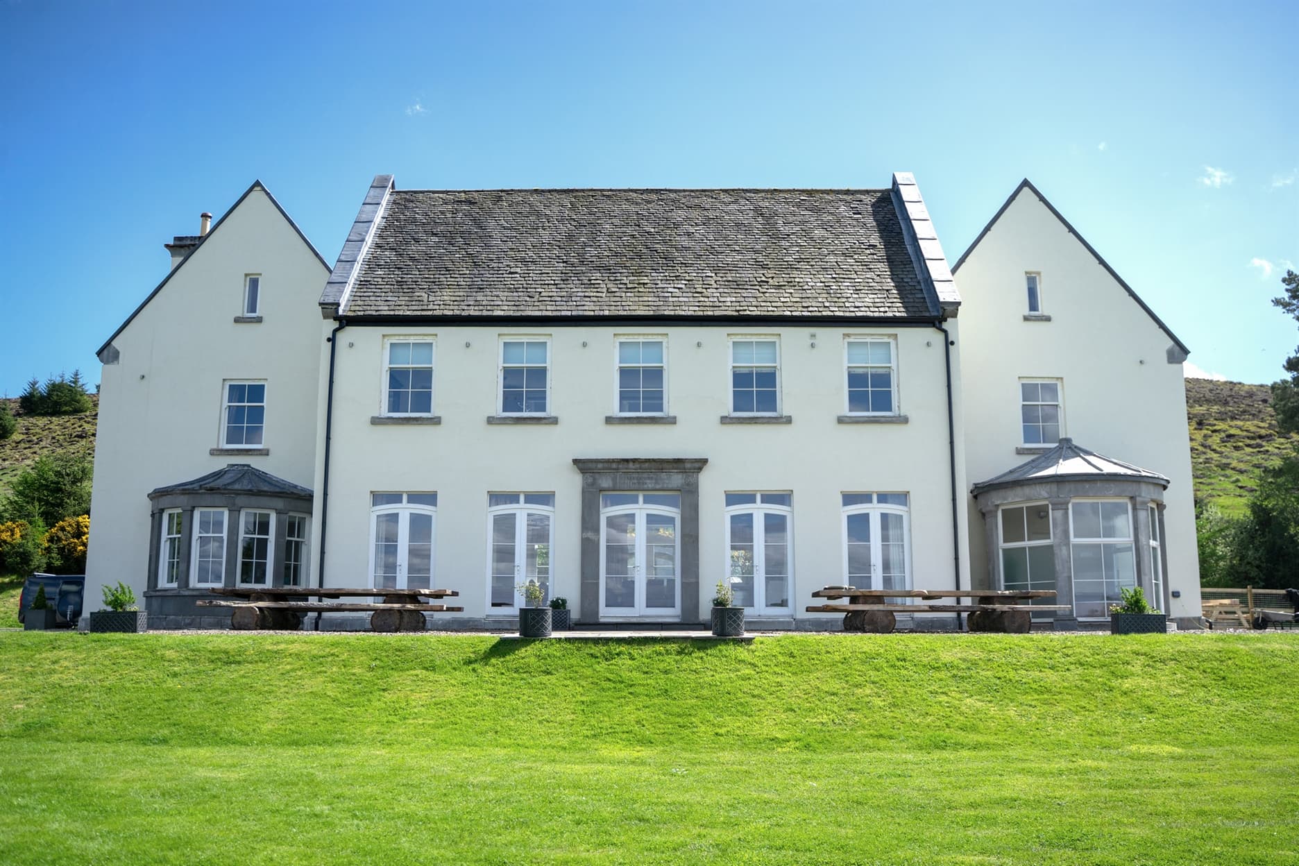 Front view of Alexander House, a large white country house with lush green lawns.