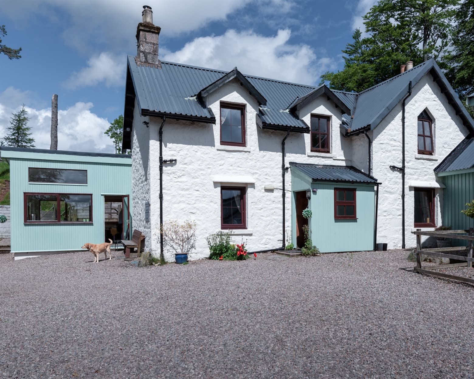 A large white washed stone building with a modern extension on the left hand side. There is a large gravel area in front of the lodge.