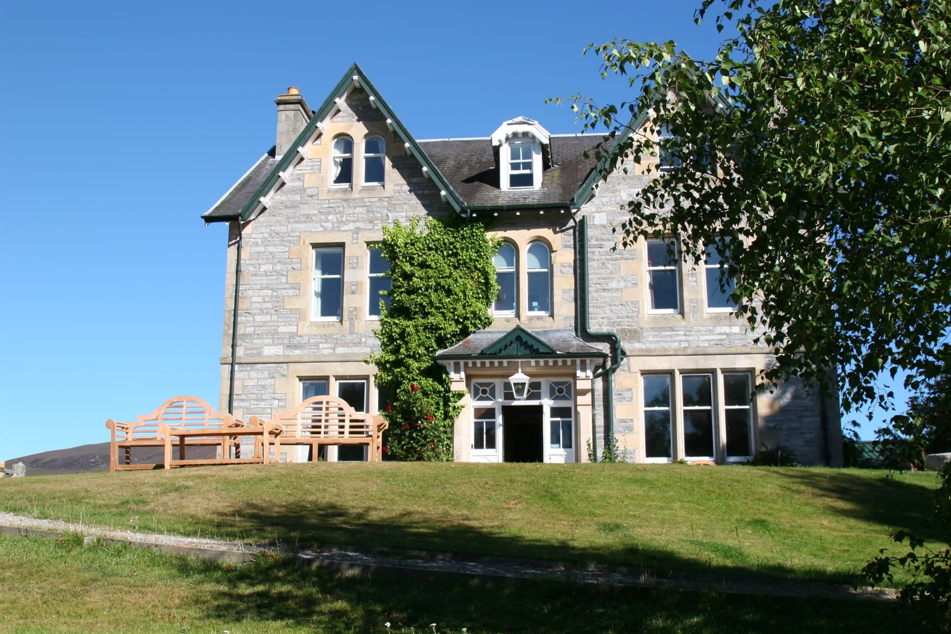 Taken from the bottom of the garden this a view of the front of the lodge. It is a large Victorian mansion house with a lawn and picnic benches at the