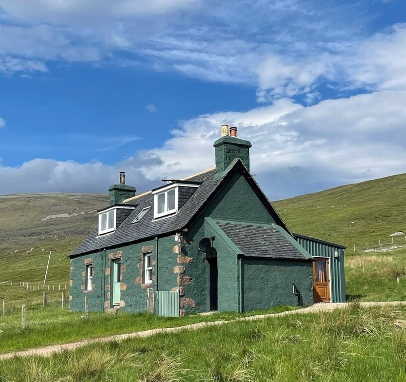 Picture of the outside of Carbreck Cottage.  It is an original shepherds cottage, painted a dark green, and surrounded by grassland fields.
