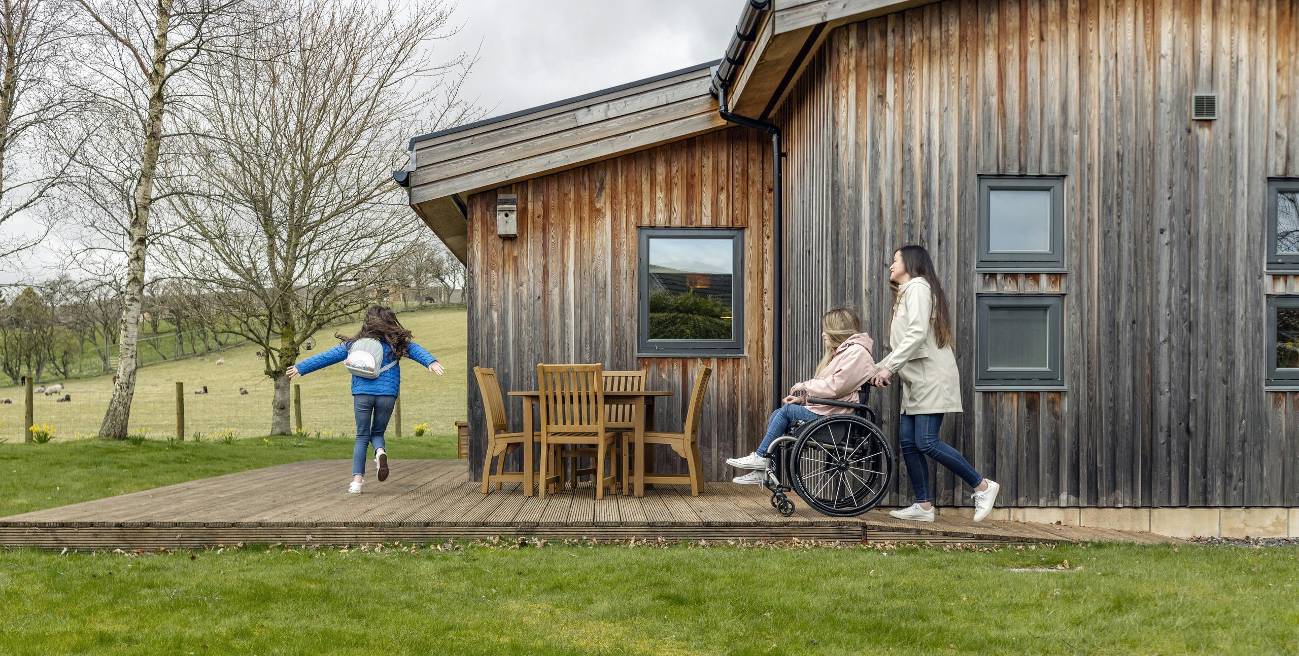 Family walking around the side of a lodge, with person in a wheelchair